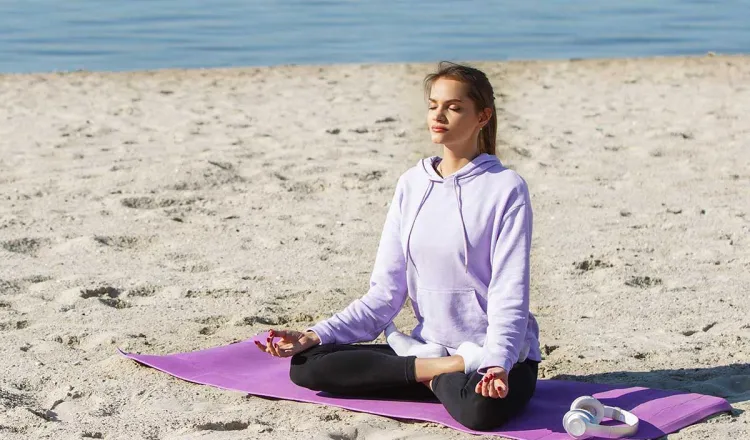 Frau meditiert beim Yoga am Strand auf Rügen mit der Ostsee im Hintergrund im Urlaub im Grand Hotel Binz.