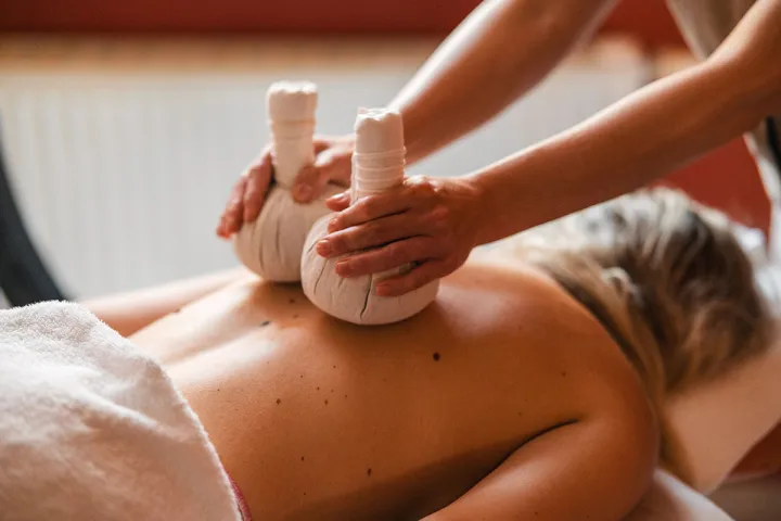 Ein weiblicher Gast erhält eine Kräuterstempelmassage nach ayurvedischer Tradition im Hotel-Spa.