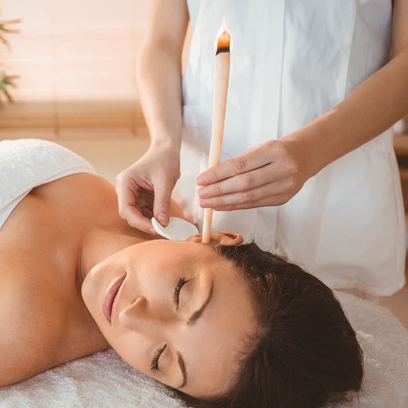 Anwendung einer traditionellen Ohrenkerzentherapie zur Linderung bei Beschwerden im Stirn-, Hals-, Ohren- und Nebenhöhlenbereich.