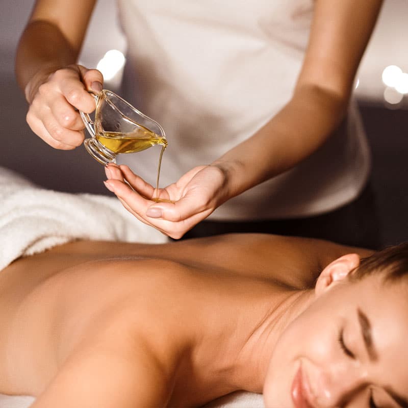 Therapeutin hält wohltuendes Massageöl über dem Rücken für eine entspannende Thai-Ölmassage.