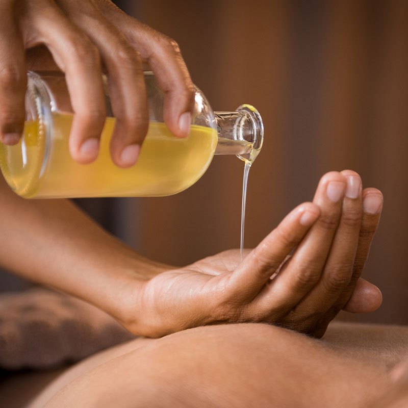 Massage-Therapeut bereitet Ölmassage vor – sanfter Start einer Wellnessbehandlung mit einer vielfältigen Auswahl an Düften.
