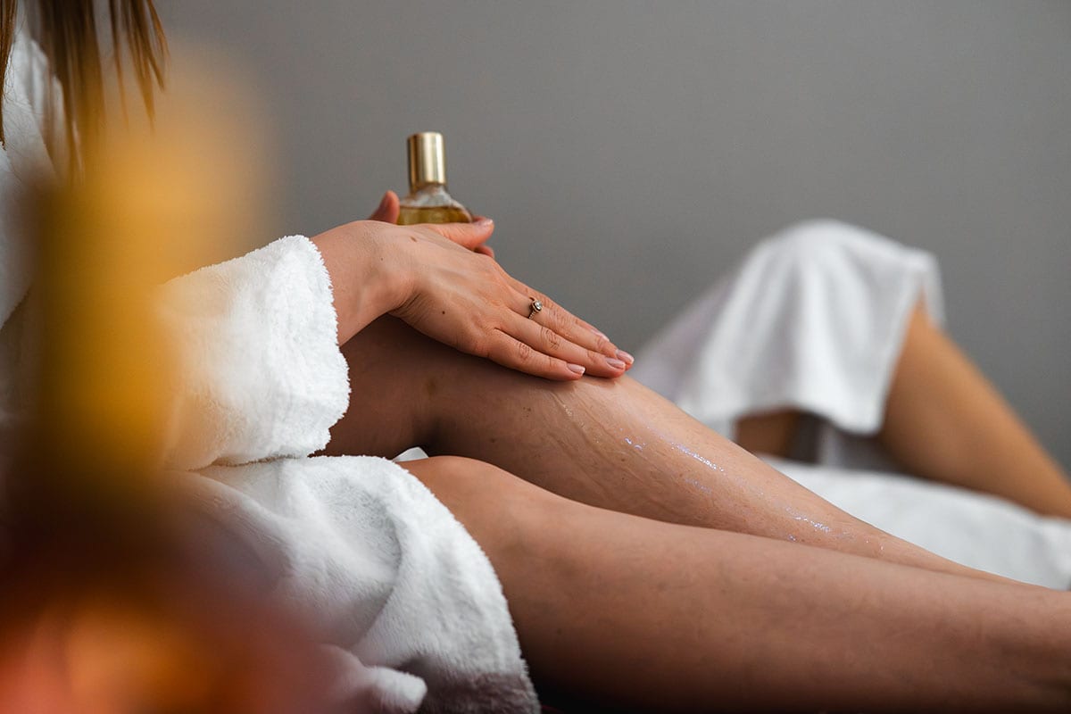 Detailaufnahme einer Wellnessbehandlung, bei der Hautöl sanft auf das Bein aufgetragen wird
