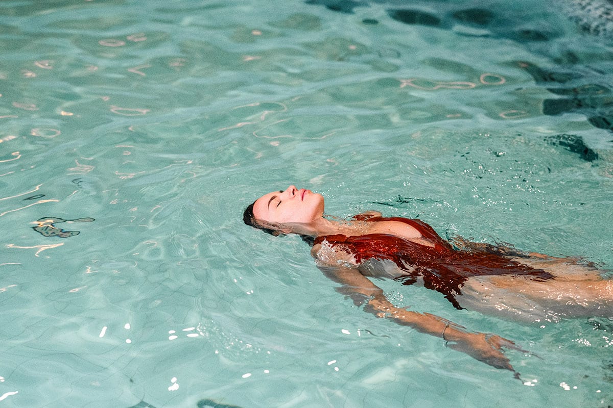 Frau in rotem Badeanzug schwebt entspannt im Pool, Wasser reflektiert sanft das Licht