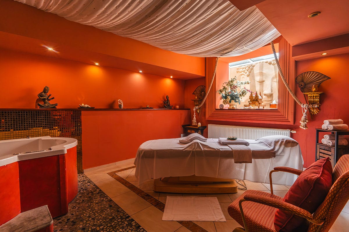 Massageraum mit Buddha-Relief, orange-farbener Wandgestaltung und dekorativen Figuren im Spa
