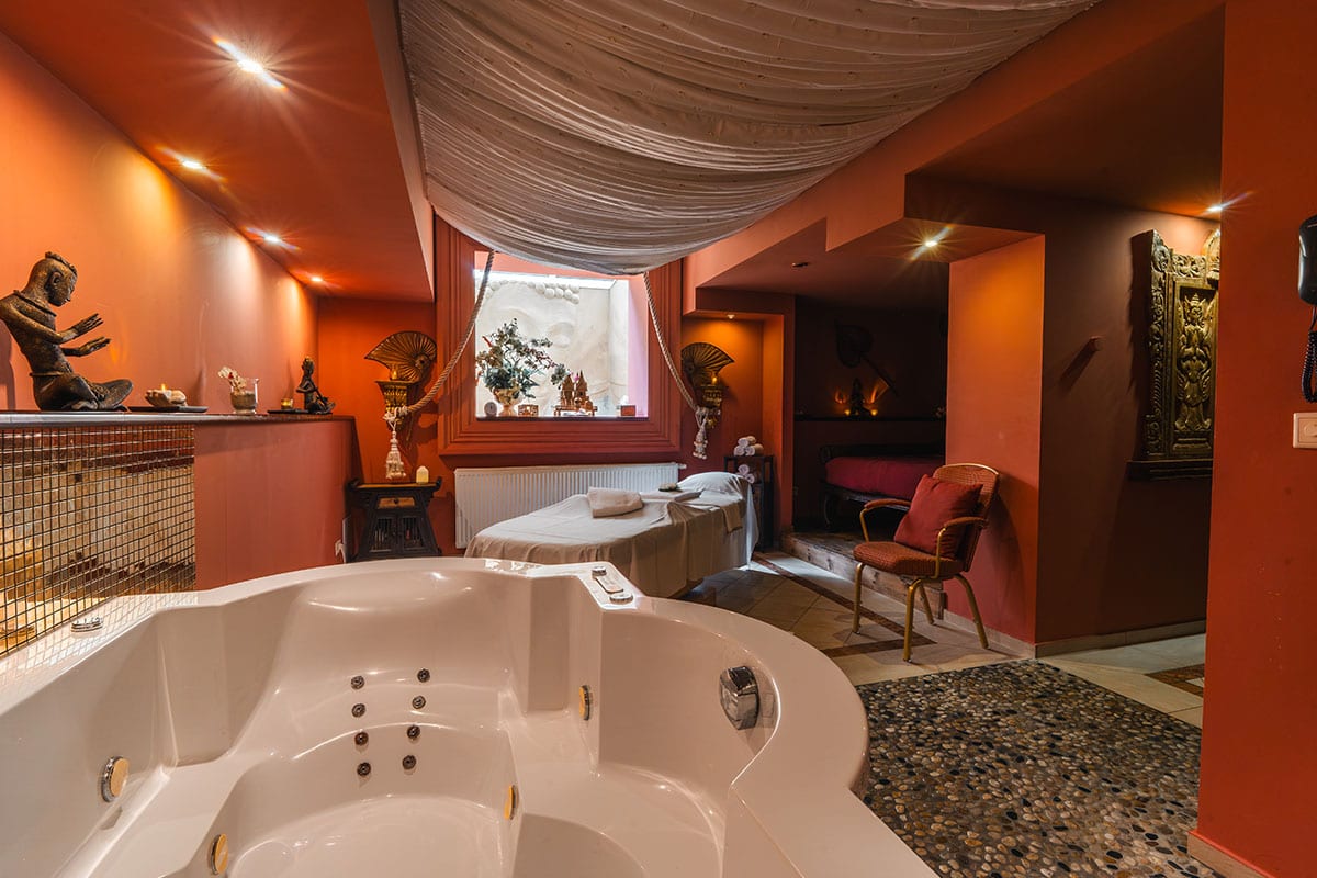Luxuriöser Behandlungsraum im Spa mit Whirlpool, Liege, asiatischer Dekoration, warmen Wandfarben und einem weißen Stoffhimmel, der die Decke ziert